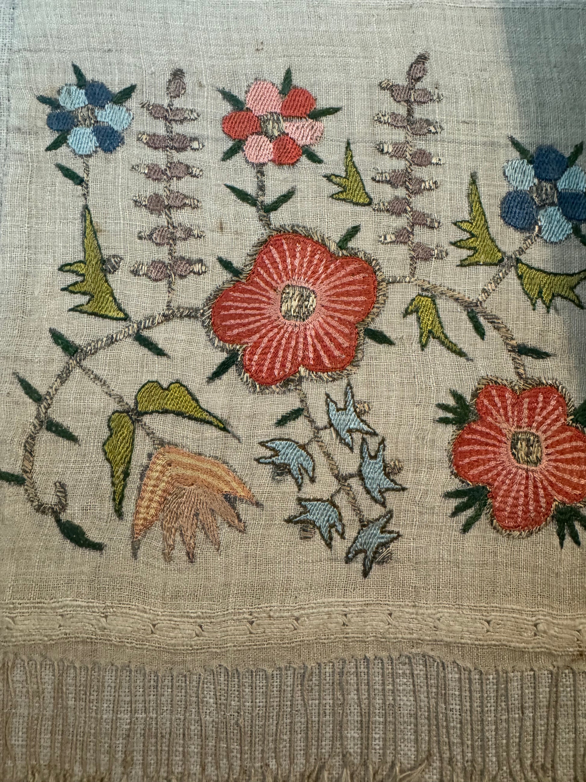 Embroidered fabric with floral patterns and small figures on a textured background