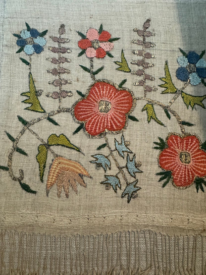 Embroidered fabric with floral patterns and small figures on a textured background