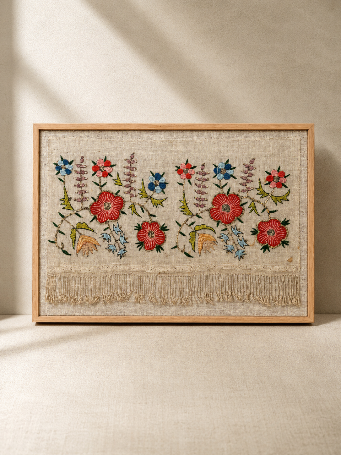 Framed embroidered artwork with floral patterns on a beige background