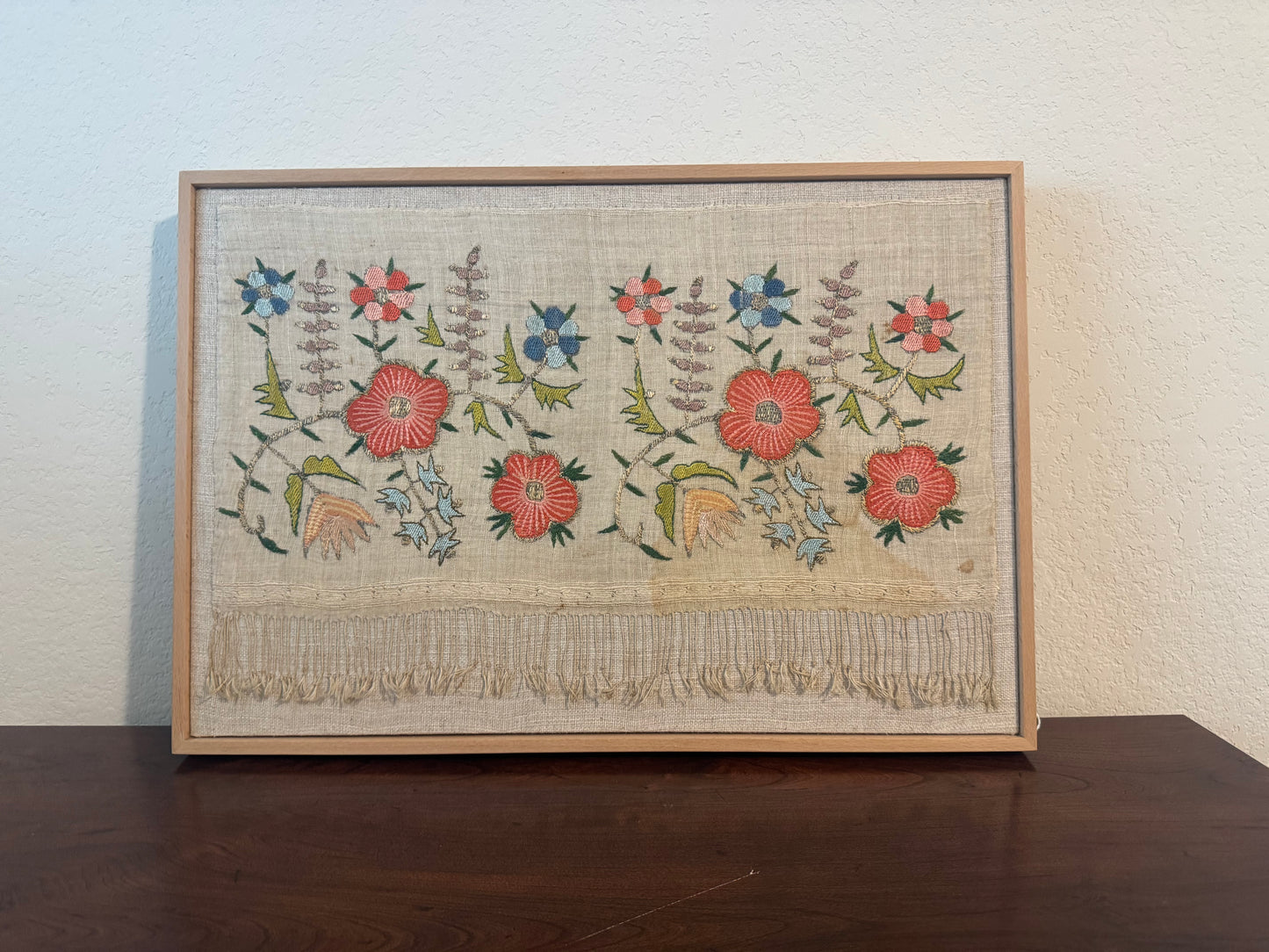 Framed embroidered artwork with floral patterns on a wooden table.