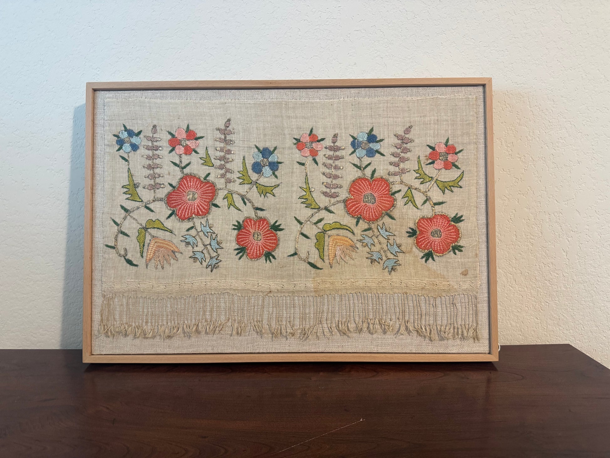 Framed embroidered artwork with floral patterns on a wooden table.