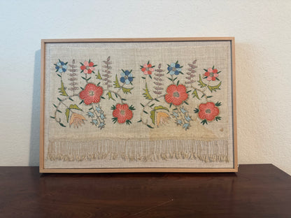 Framed embroidered artwork with floral patterns on a wooden table.