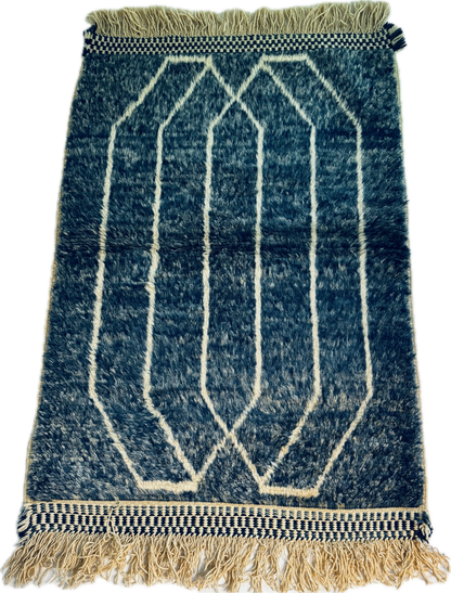 Blue and white geometric patterned rug with fringes on a plain background